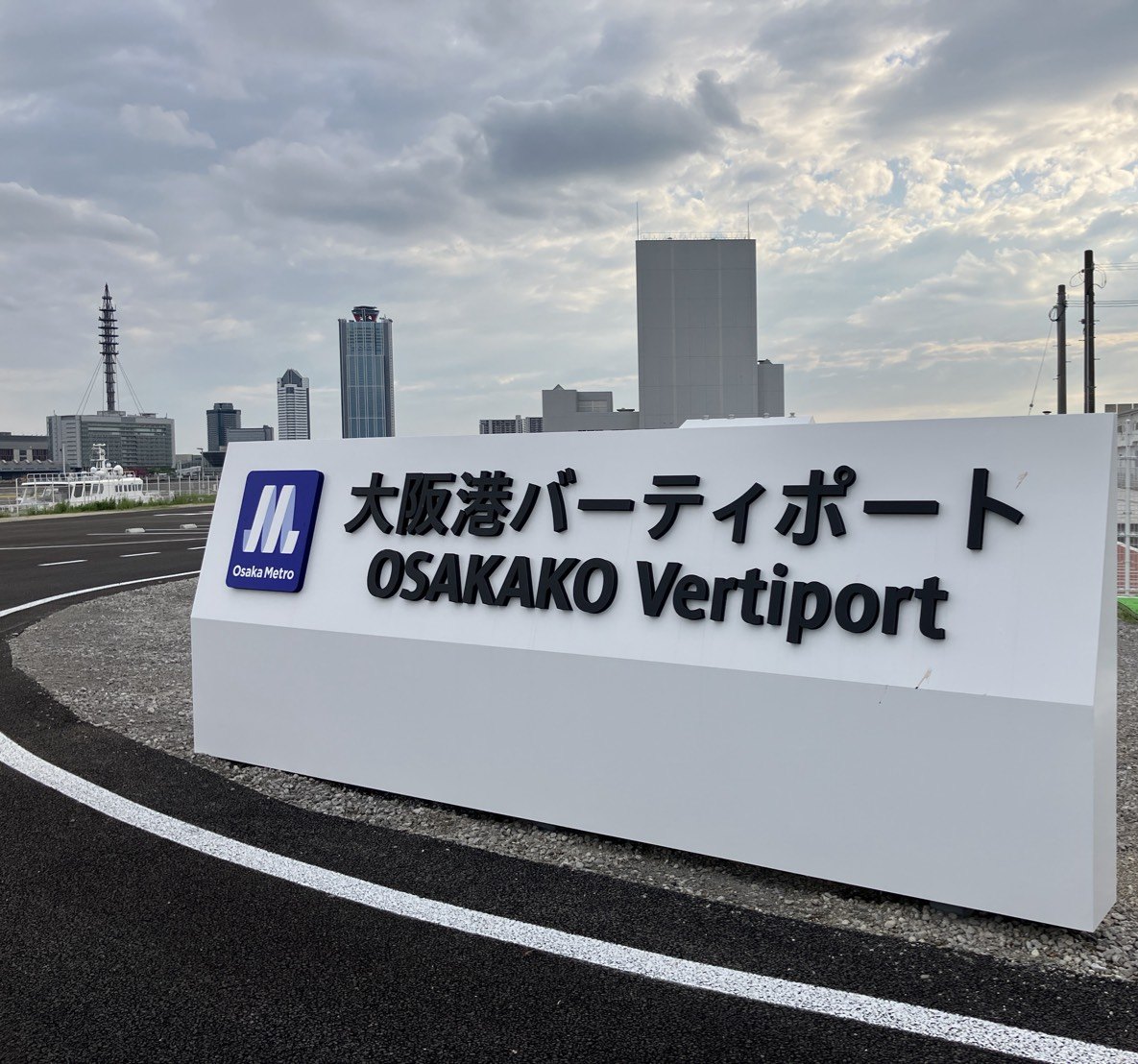 Osaka Metroのロゴと「大阪港バーティポート OSAKAKO Vertiport」と書かれた白い看板。後ろに大阪港の建物が並ぶ